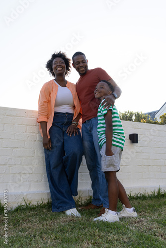 African American family standing on grass in front of low white brick wall, smiling