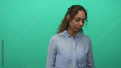Konstfotografi Young woman looking down with visible face in a bright teal studio setting, soft lighting and neutral expression; contemplation
