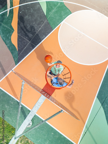 vertical aerial view Two active elderly men playing a game of basketball on an outdoor court, seen from a high angle directly above the hoop, showcasing sport for older adults