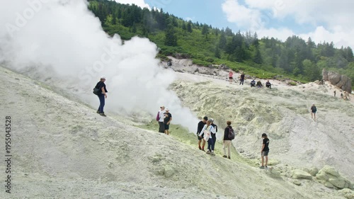 Group of hikers stand near the smoking fumarole on the active volcanic area on Kunashir Island in Russia