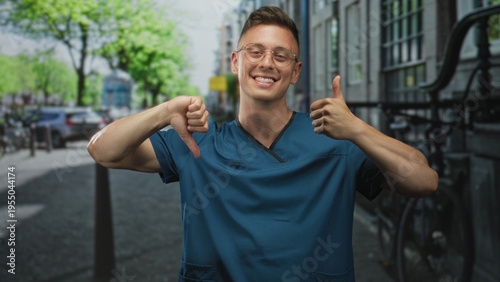 Man doctor in blue medical scrubs smiling with glasses showing thumbs up and thumbs down while standing on a street; ambivalence choice.