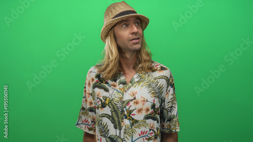 Фотография Man with long hair wearing straw hat and tropical shirt looking up in green studio; wanderlust vacation
