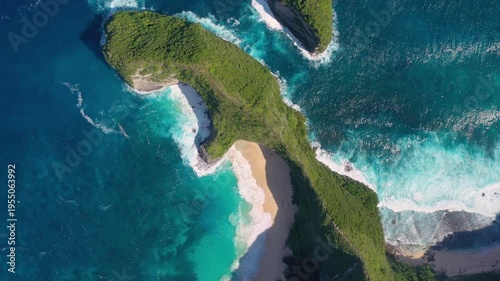 Aerial drone footage of Kelingking Beach in Nusa Penida, Indonesia. Massive turquoise waves crash on the sandy shore below the iconic T-Rex shaped cliff. Stunning view of the secluded cove.