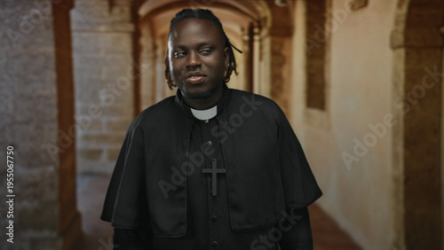 Photos Man priest with cross necklace holds finger to lips for silence in a building corridor; quiet reflection serenity