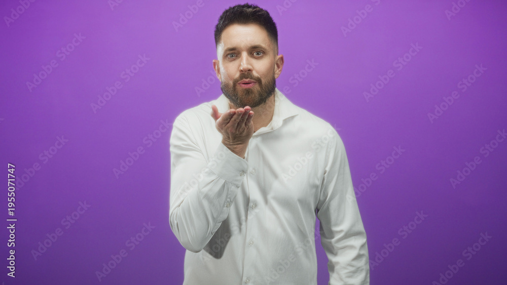 Obraz premium Man blowing a kiss with hand visible, smiling and wearing a white shirt against a purple studio backdrop; playful.