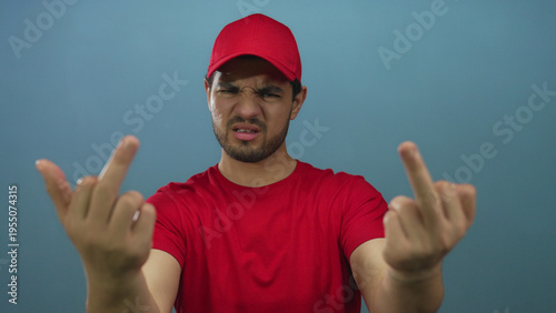 Fotografía Hispanic man in red shirt and cap raising two middle fingers for insult gesture in studio; defiance