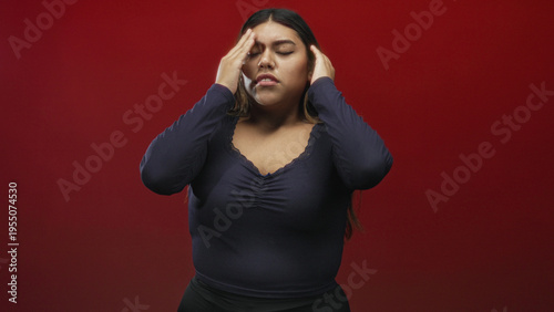 Woman pressing hand to forehead with eyes closed showing headache and subtle grimace in studio; fatigue and coping.