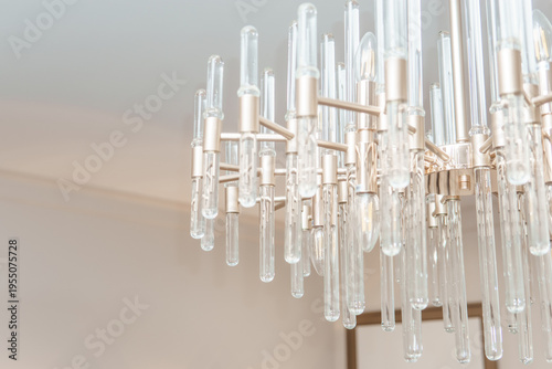 Modern glass chandelier with metal frame hanging in bright living room. Elegant ceiling lamp for home interior design. Luxury decorative lighting fixture for contemporary apartment decor.
