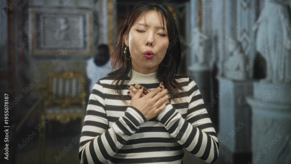 Fototapeta premium Woman with hands on chest and closed eyes in ornate museum building, striped sweater and visible rings; reverence.