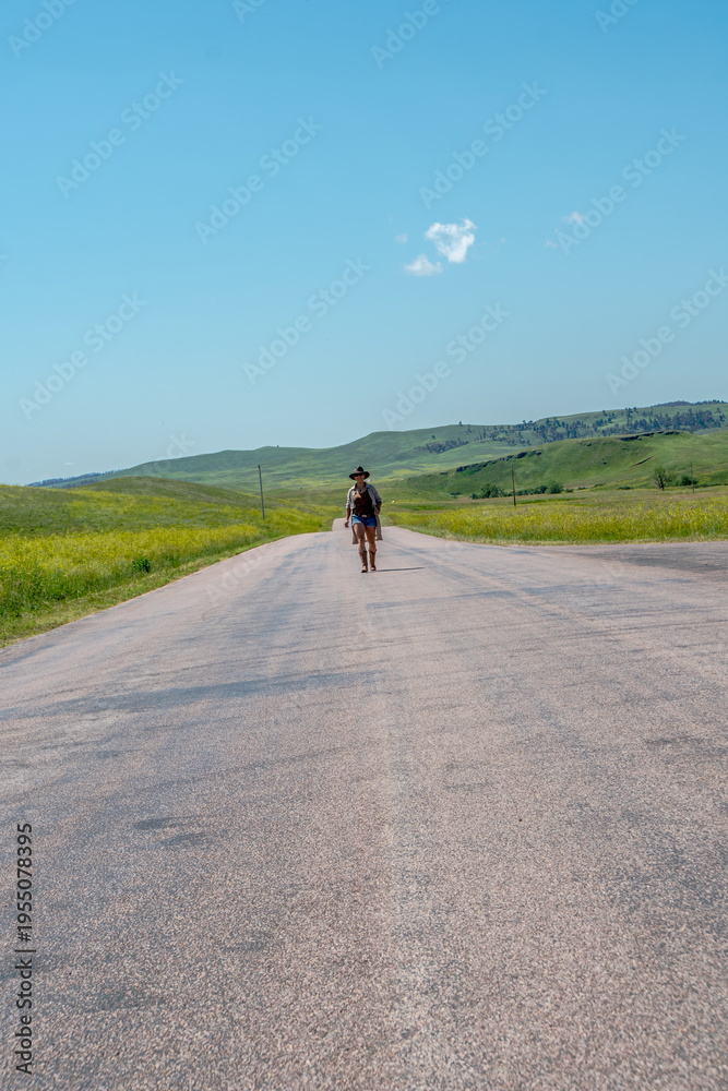 Obraz premium Single traveler walks down quiet rural road under clear blue sky