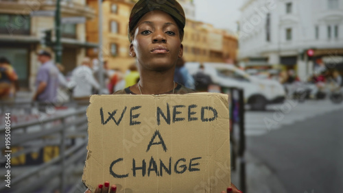 Tableau sur toile Woman soldier wearing camouflage uniform holding cardboard protest sign on busy urban street; determination change activism