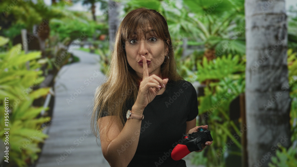 Fototapeta premium Woman holding a game controller and finger to lips for silence in forest; playful gentle secrecy hush.