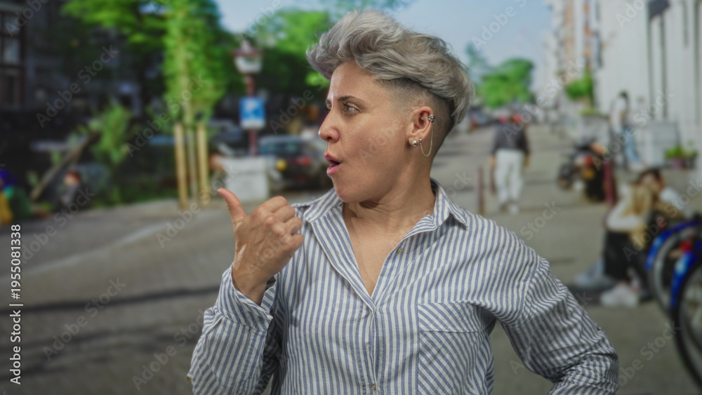 Fototapeta premium Woman in striped shirt pointing thumb on busy street lined with bicycles and parked cars; surprise.