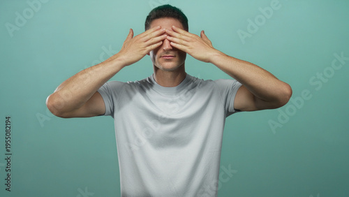 Foto Young man covering eyes with hands in studio against mint green wall wearing gray tshirt; introspection privacy