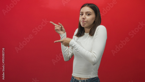 Wallpaper Mural Young woman points index fingers to the right against a studio red backdrop while wearing a white shirt and jeans; playful confidence. Torontodigital.ca