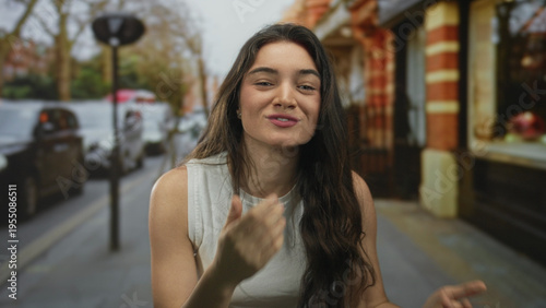 Canvas-taulu Young hispanic woman playfully blowing a kiss towards camera on a vibrant city street; warm affection