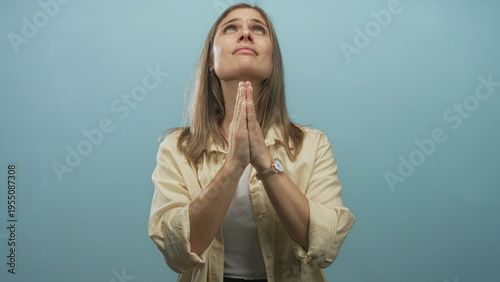 Принти на полотні Woman with blonde hair praying with hands pressed together in studio against a light blue background; devotion