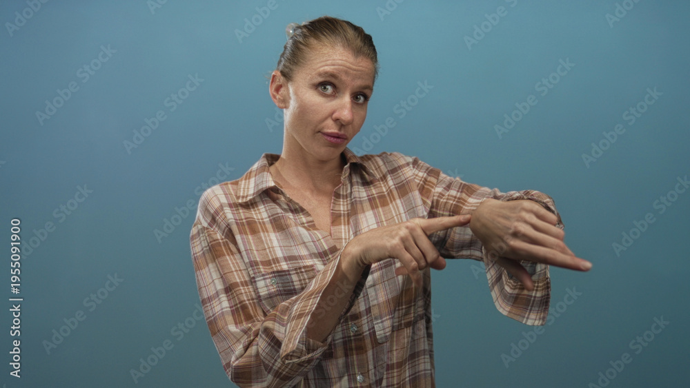 Αυτοκόλλητο Woman points finger to wrist in studio against blue background while tapping her hand over a plaid shirt, signaling time and attention; impatience urgency
