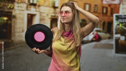Quadro su tela Woman holding vinyl record with hand on head and pink sunglasses on a cobbled street; nostalgia retro
