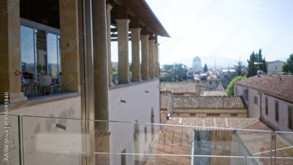 Obraz premium Sunlit terracotta rooftop view with distant dome, defocused balcony columns and glass railing, soft blurred skyline city; background backdrop copyspace calm.