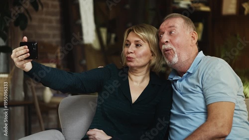 Cheerful senior man and his grown-up daughter taking selfie on phone, having fun