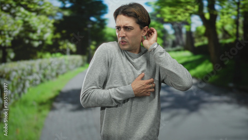 Photos Man clutching chest and recoiling on a tree lined street, hands near ribs and tense expression; alarm vulnerability