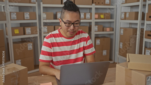 Wallpaper Mural Man in striped shirt typing on laptop among parcel boxes with a fist pump gesture in storage building; small business success. Torontodigital.ca