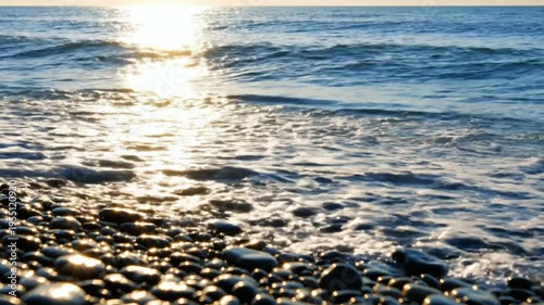 Sparkling waves crashing on a pebble beach at sunrise reflecting golden sunlight and ocean views