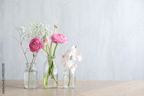 Beautiful flowers in vases on wooden table against light background. Space for text
