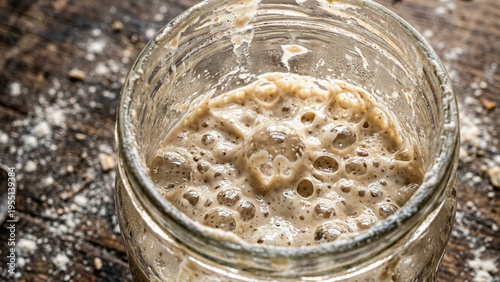 Close-up of active sourdough starter with bubbles in glass jar, artisan baking process