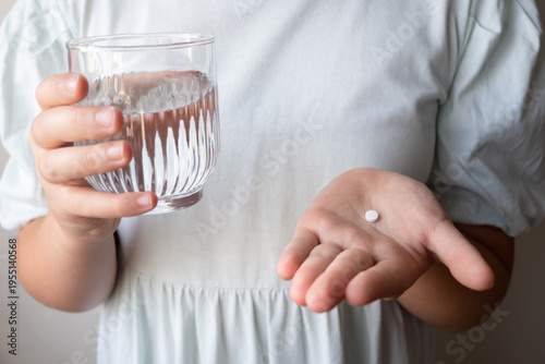 Girl is ill and stay at home. Kid holding pill and glass with water in the hands.