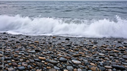 Waves Crashing on a Pebble Beach with Grey Cloudy Skies Depicting a Dramatic Coastal Scene