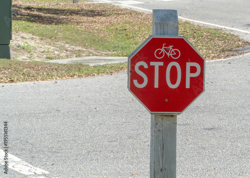 Red Bicycle Stop Sign on a Weathered Wooden Post Along an Asphalt Path with Grass and Scattered Leaves, Emphasizing Cycling Safety and Traffic Regulations.