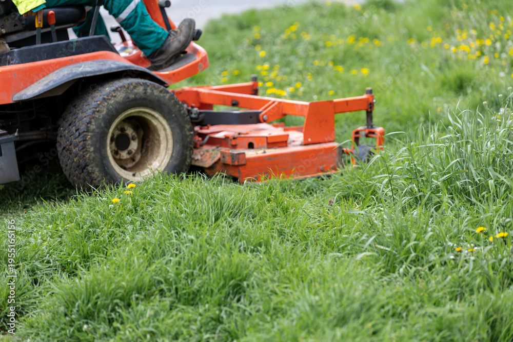 Obraz premium Ride on mower cutting tall grass in spring meadow area