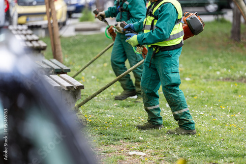 Foto Groundskeepers trimming grass in urban park with brush cutters
