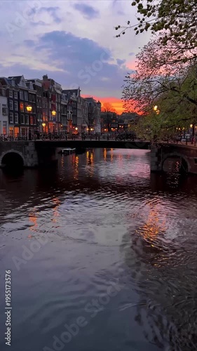 View of an Amsterdam canal with historic bridges, traditional dancing houses  against a stunning colorful sunset sky, Netherlands.