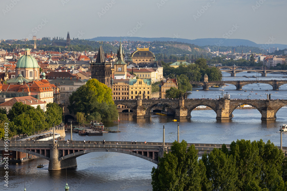 Obraz premium Aerial view of historic Prague showcasing the Vltava River, iconic bridges, and colorful architecture under a clear blue sky in the Czech Republic