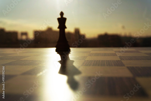 фотографія A dramatic cinematic shot captures a lone chess king piece in silhouette against a blurred city skyline during sunrise