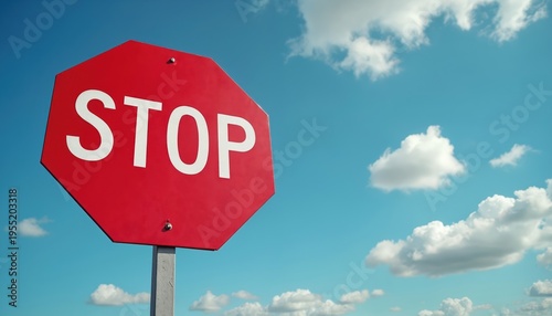 Red octagonal stop sign stands against clear blue sky with white clouds. It indicates a halt, emphasizing traffic regulations and road safety directives.