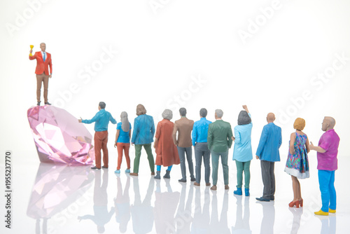 Miniature people celebrate around a large diamond-shaped crystal on a white surface during a gathering event