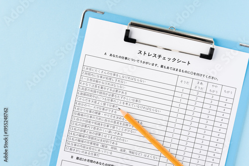 水色背景にバインダーに挟んだストレスチェックシートと鉛筆