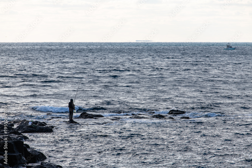 Obraz premium idyllic seascape with a man fishing on the rocky shore in Jeju Island, South Korea