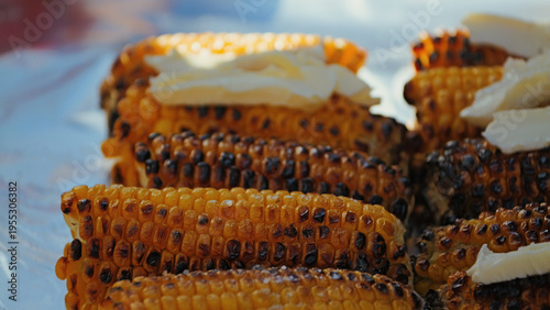 Close-up of freshly grilled corn on the cob with butter melting over warm, charred kernels. Shallow depth of field natural light highlight the savory texture. A classic food festival barbecue snack