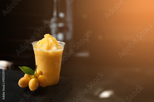 Marian plum smoothie in a clear plastic cup with fresh marian plums on a café counter, highlighted by warm natural light and soft bokeh background.