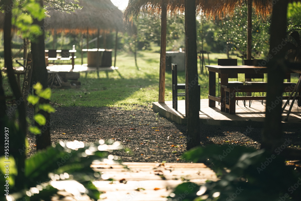 Fototapeta premium Outdoor cafe garden table wooden chair sunlight summer green nature grass relax leisure countryside outdoor cafe with wooden table and chair straw roof warm sunlight, peaceful garden setting with