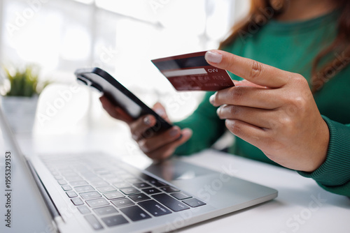 Fotografie This image portrays a person holding a mobile phone and a credit card, focused on typing on a laptop, illustrating the seamless blend of technology in daily routines