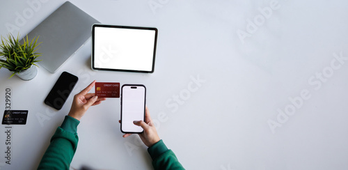 A person is holding a credit card while using a mobile device, depicting an online transaction process in a modern setting with a laptop nearby.