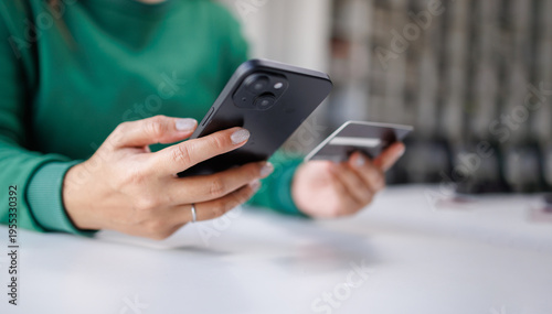A person is engaged in a financial transaction with a smartphone in one hand and a credit card in the other, showcasing modern online shopping habits and technology.