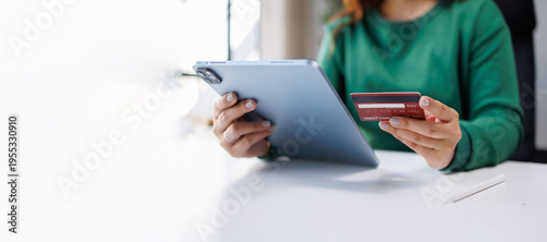 Obraz na plátně An individual is securely holding a tablet along with a red credit card, ready to make a purchase, representing the modern consumer's experience in digital commerce
