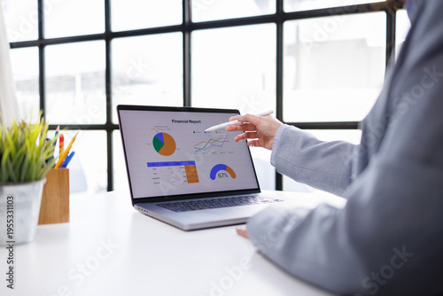A professional points decisively at a financial report on a laptop, emphasizing key data points and trends important for strategic business planning and financial insights.